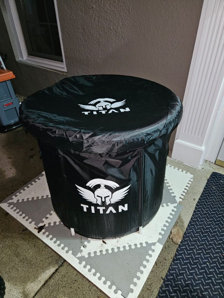 Customer review photo of Titan Bravo cold plunge with protective cover outdoors, round black tub on foam floor tiles near house wall