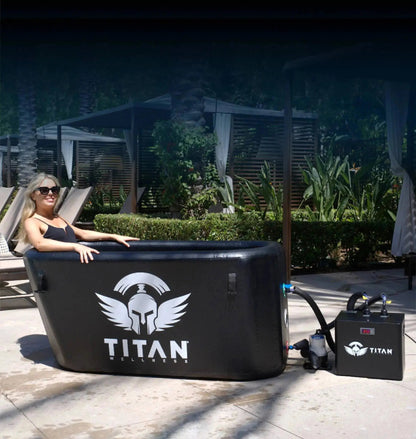 “Triumph XL cold plunge in black connected to the Titan water chiller, shown in use outdoors with a woman relaxing in the tub on a sunny patio.”